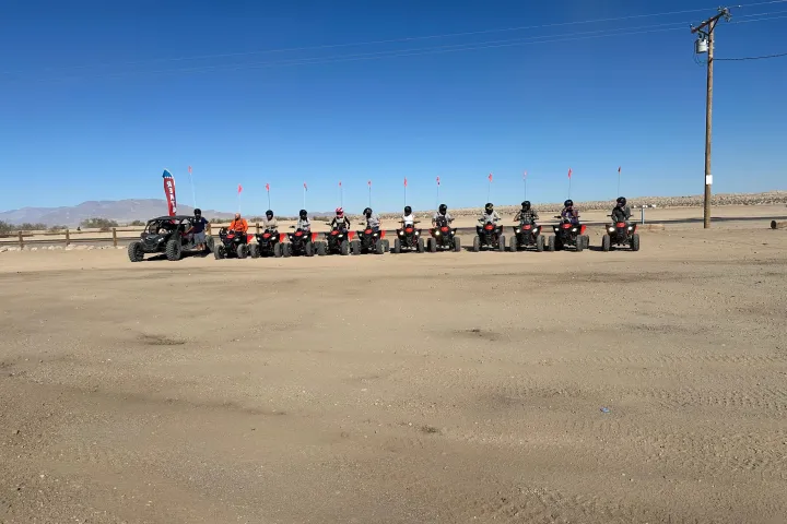 Line of ATVs and a buggy on desert ground under a clear blue sky.
