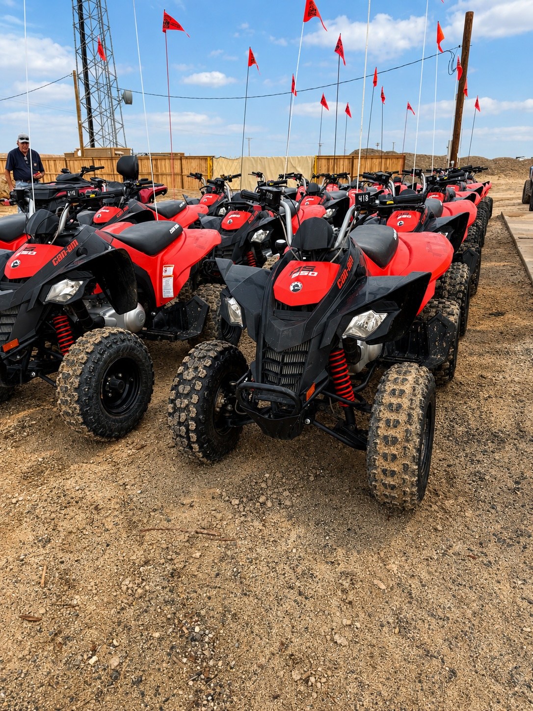 Rows of red and black ATVs parked on sandy ground with flags on poles.
