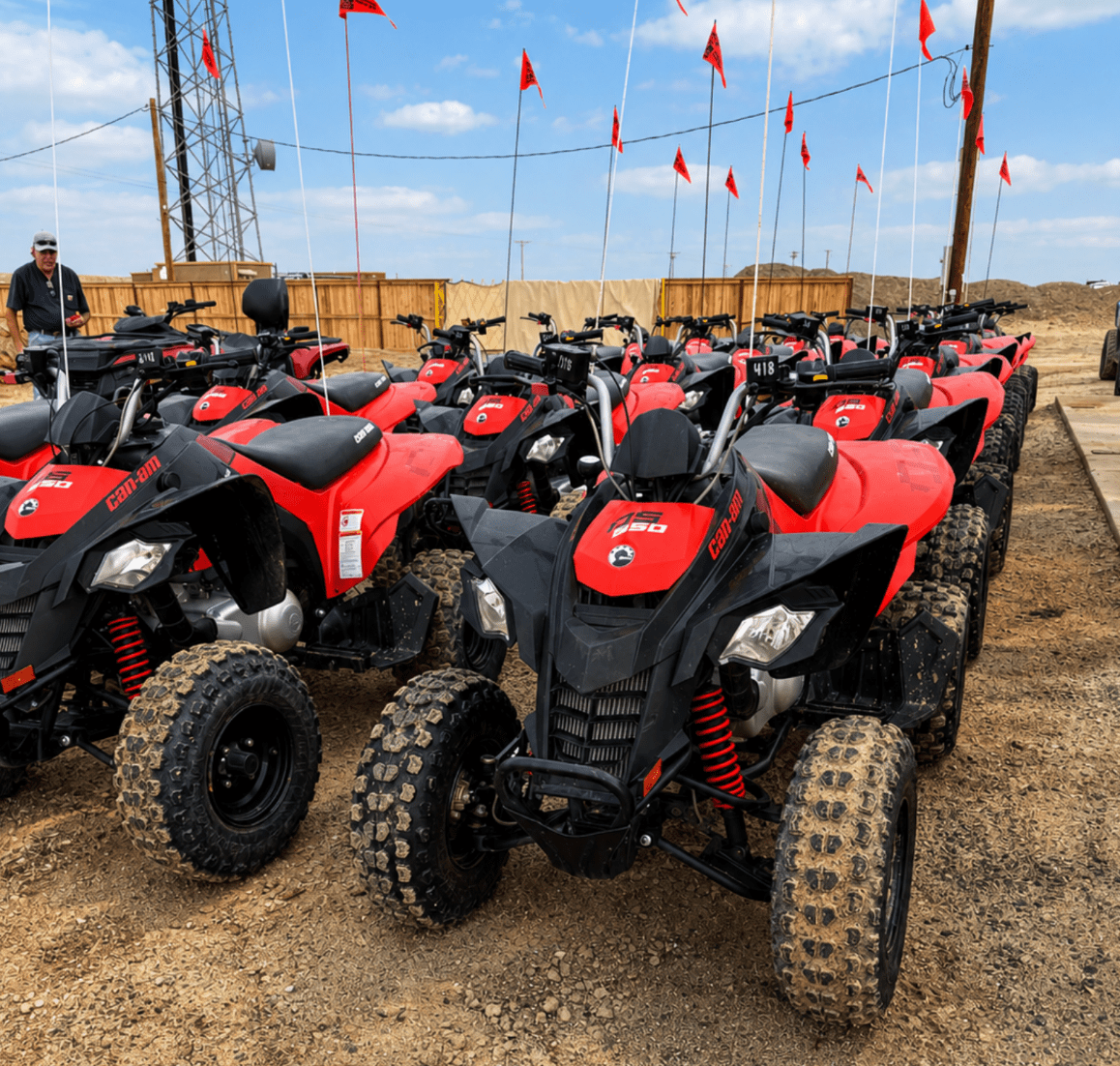 Rows of red and black ATVs with flags in a dirt area.