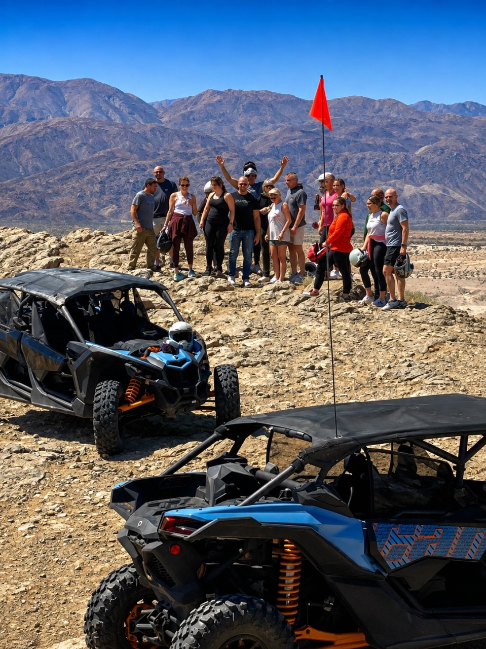 Group posing on rocky terrain with two off-road vehicles, mountains in background.