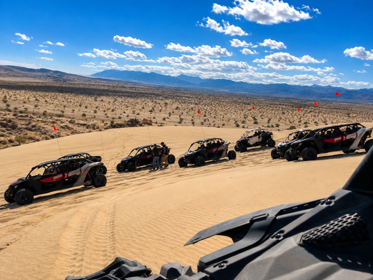Six off-road vehicles on desert sand dunes under a blue sky.